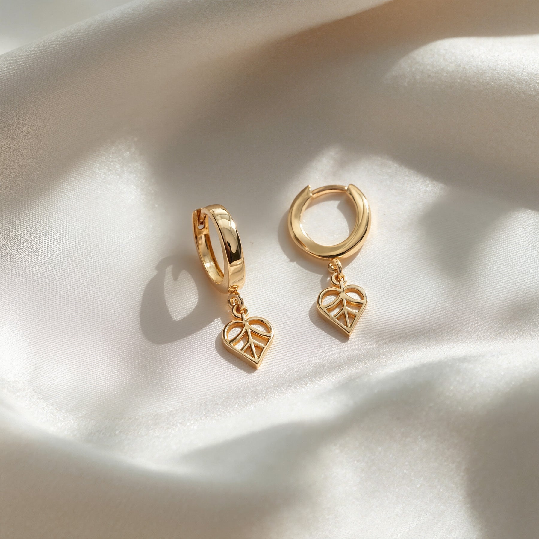 Gold hoop earrings with heart-shaped charms on a white fabric background