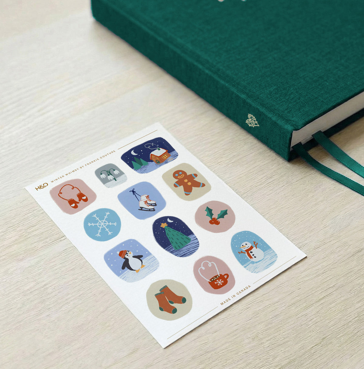 Winter Whimsy sticker sheet by Frankie Couture shown beside a notebook with one of the stickers applied