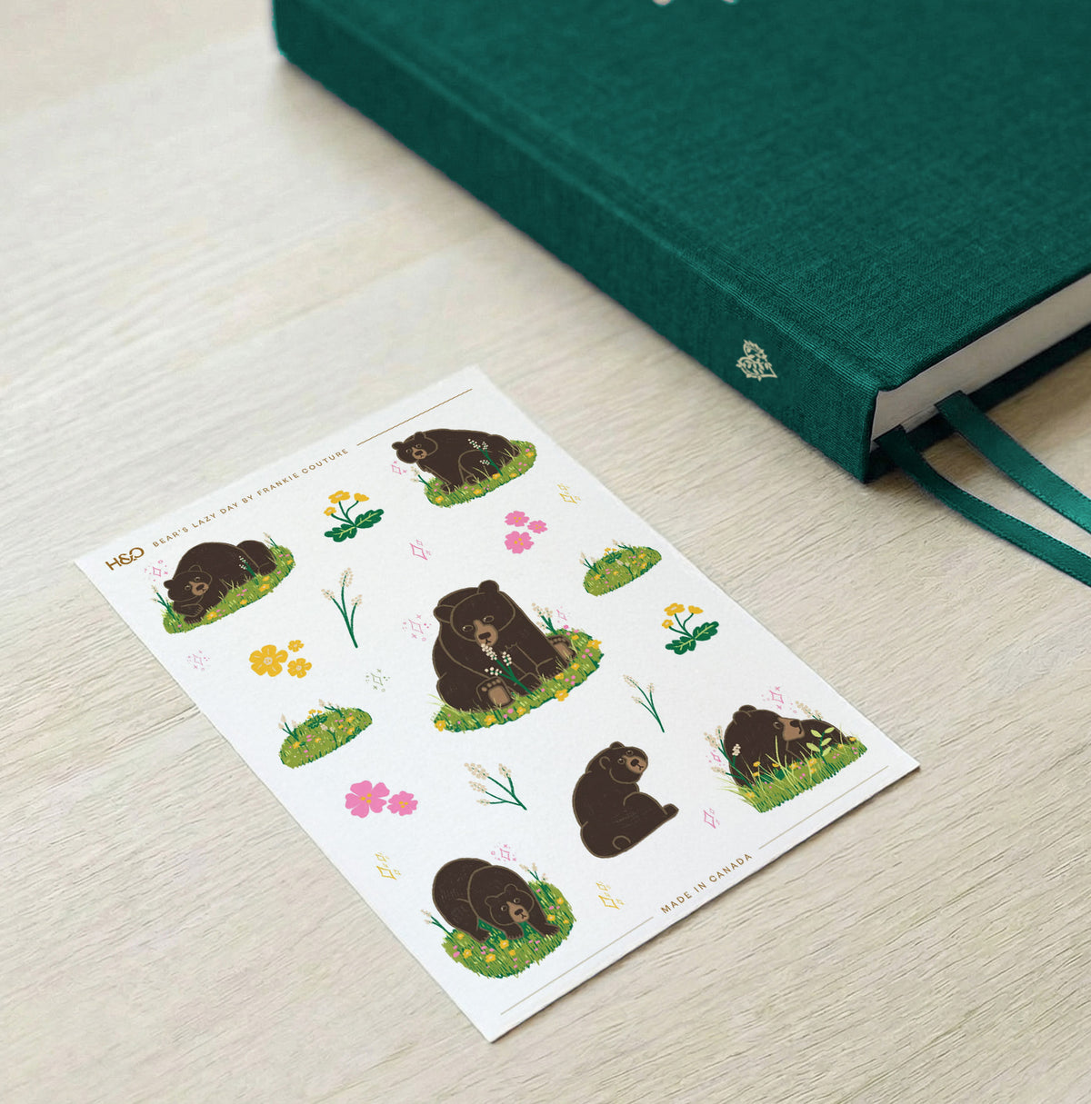 Bear's Lazy Day sticker sheet by Frankie Couture shown beside a notebook with one of the stickers applied