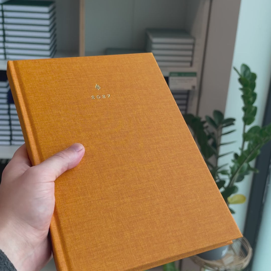 2027 B5 Minimalist Vertical Planner (Hardcover, Heritage 120gsm) in Clementine, held in hand #color_clementine