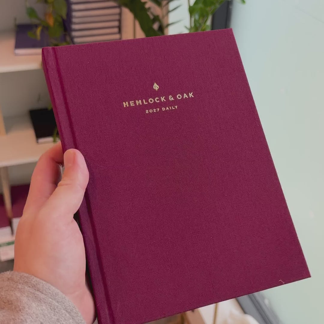 2027 Signature Daily Planner (Hardcover, A5+, Archivist 70gsm) in Mulberry, held in hand #color_mulberry