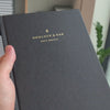 2027 Sunday Start Weekly Planner (Hardcover, Vertical, Heritage 120gsm, A5+) in Charbon, held in hand #color_charbon