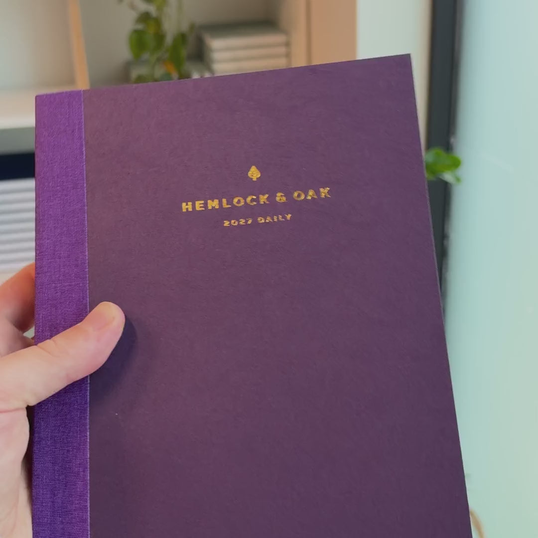 2027 Signature Daily Planner (Paper Flex, A5+, Archivist 70gsm) in Plum, held in hand #color_plum
