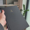 2027 B5 Minimalist Vertical Planner (Hardcover, Heritage 120gsm) in Charbon, held in hand #color_charbon