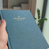 2027 Weekly Planner (Hardcover, Vertical, Heritage 120gsm, A5+) in Rivière, held in hand #color_riviere #color_rivière