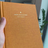 2027 Sunday Start Weekly Planner (Hardcover, Vertical, Heritage 120gsm, A5+) in Clementine, held in hand #color_clementine