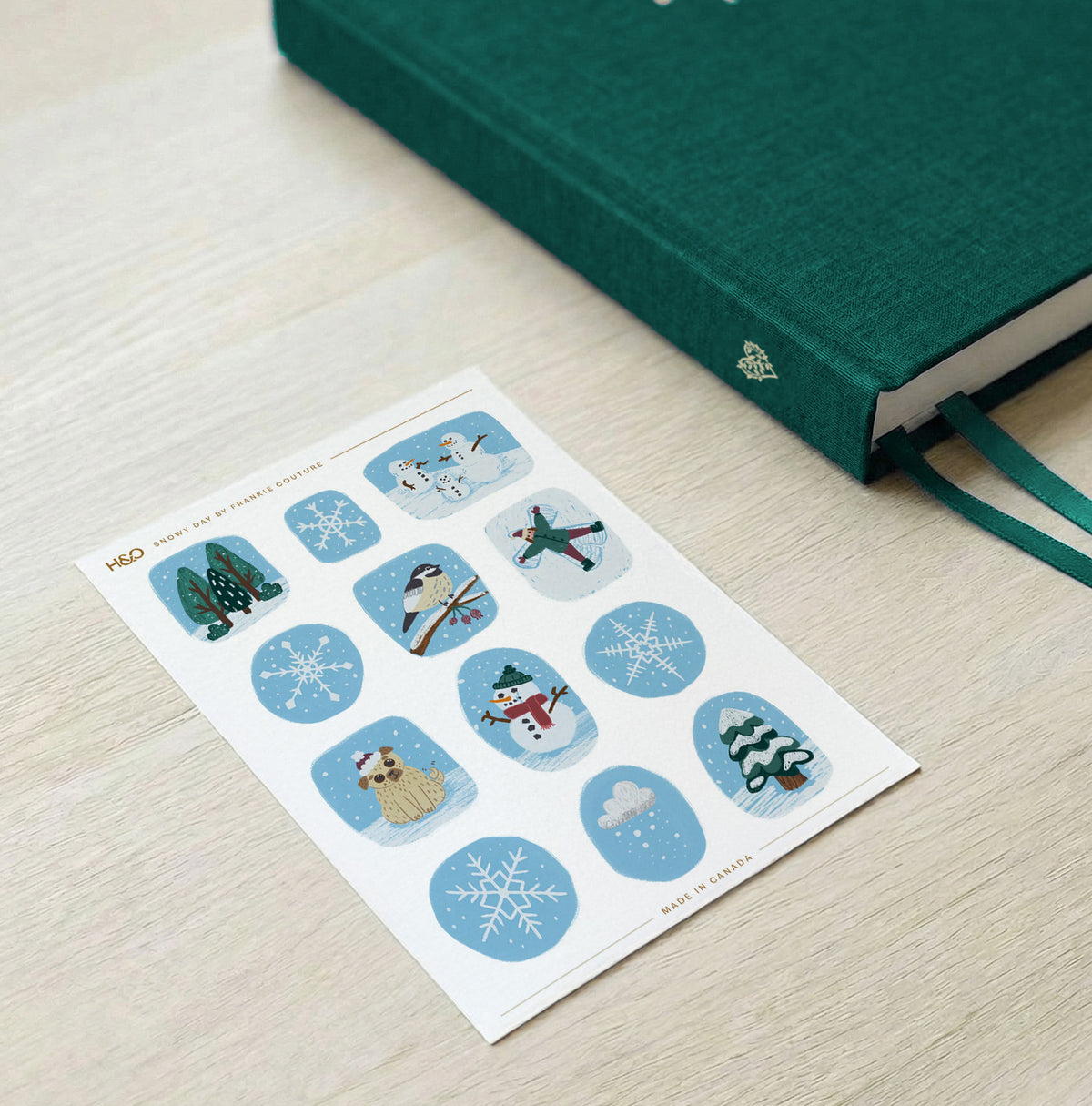 Snowy Day sticker sheet by Frankie Couture shown beside a notebook with one of the stickers applied