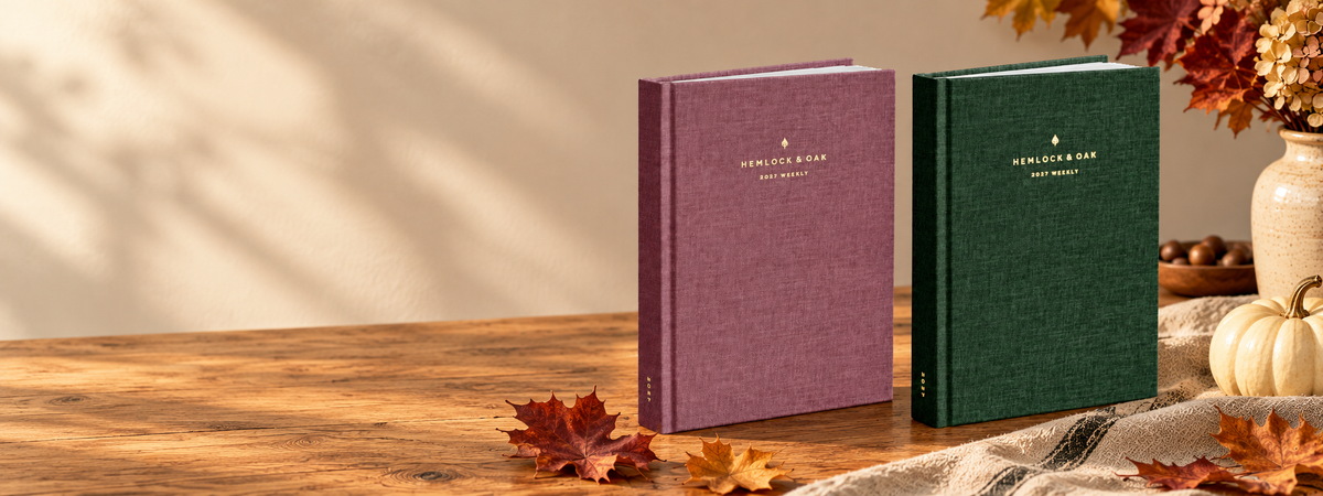 Wild Rose and Woodlands 2027 Weekly planners on a warm oak table with autumn leaves, linen and an ivory pumpkin